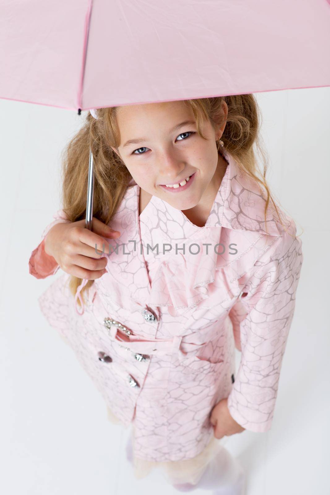 Above view of pretty girl in raincoat standing and looking up. Happy blonde preteen girl posing in studio against white background. Happy childhood concept