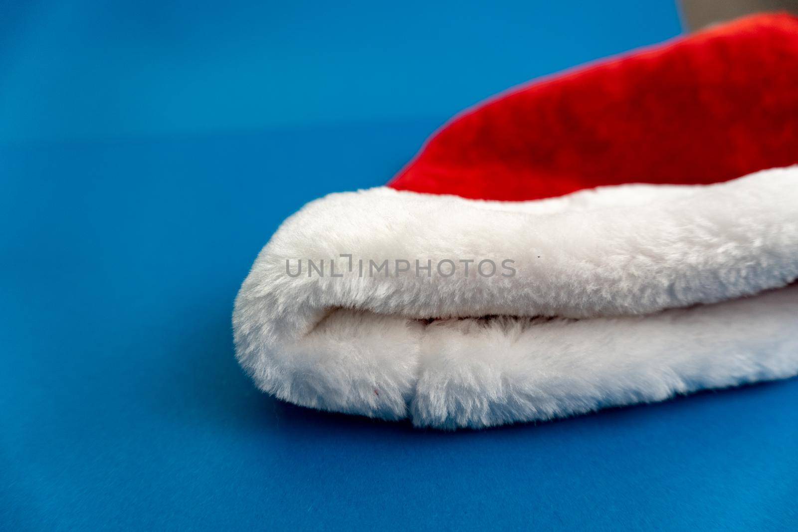 Red and white christmas santa hat lay on blue background on the rigth. Enough space for text.