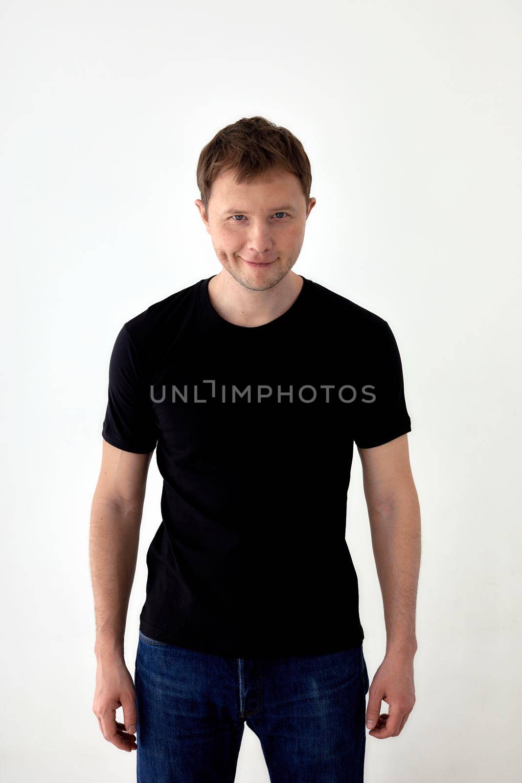 Glad young male in jeans and black t shirt standing against white background and looking at camera