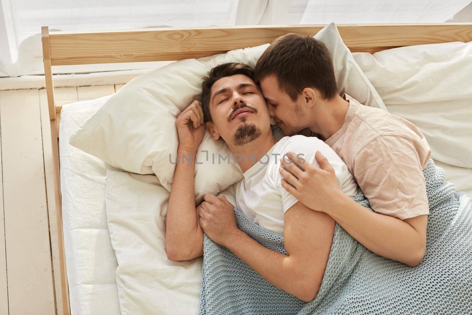 Happy gay couple lying on bed at home top view