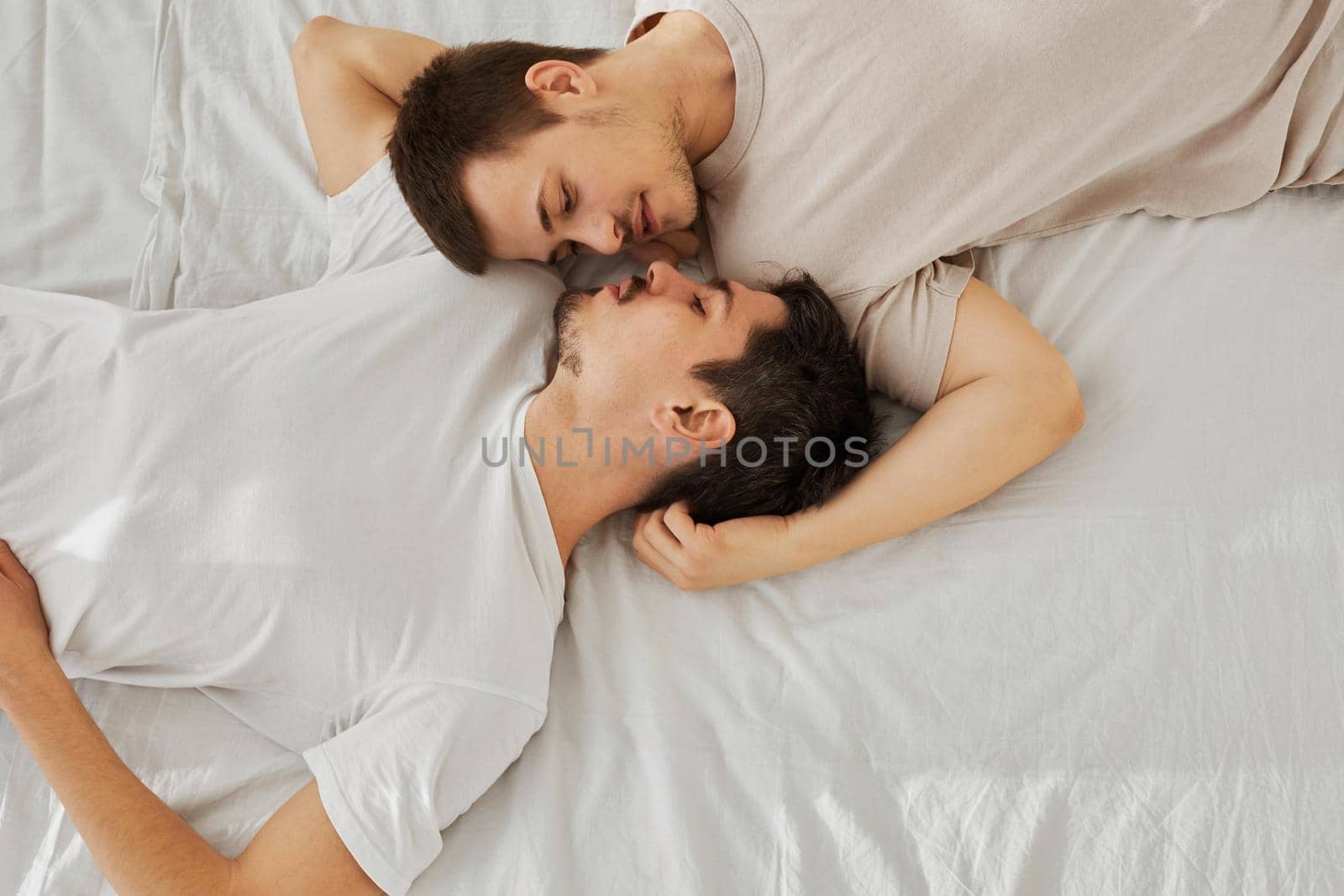 Young gay couple lying on bed head-to-toe, top view by Demkat