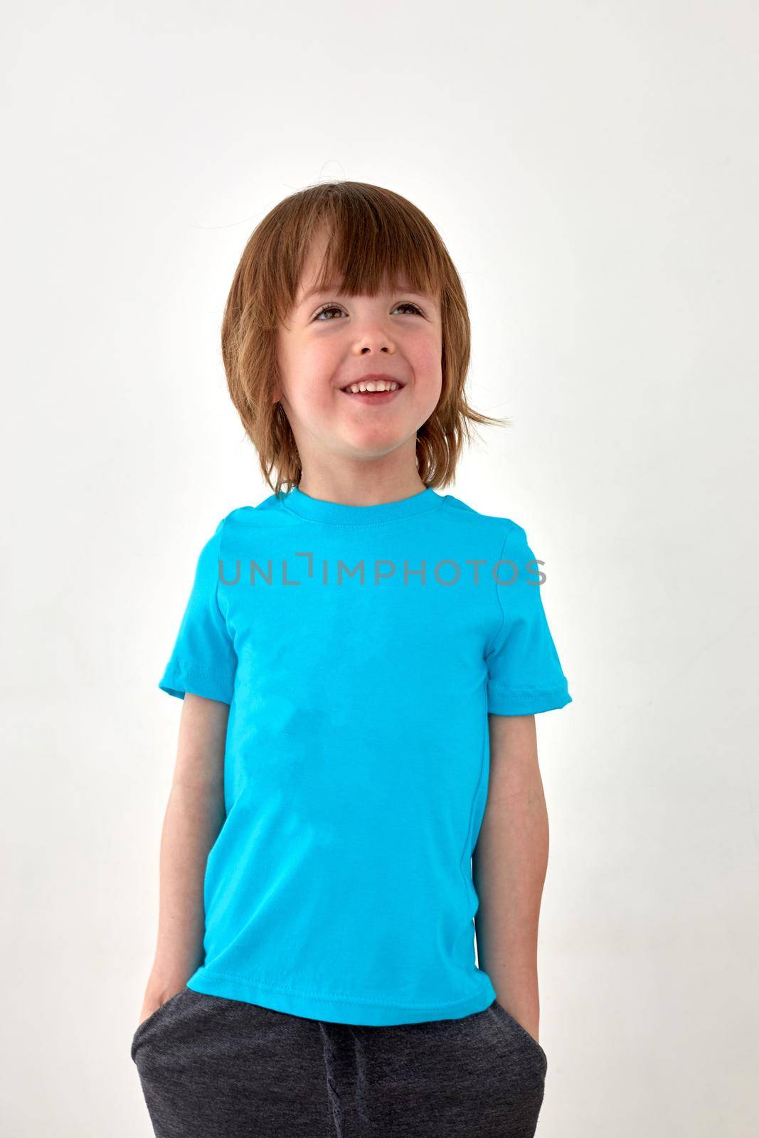Glad young boy in blue t shirt standing against white background and looking away