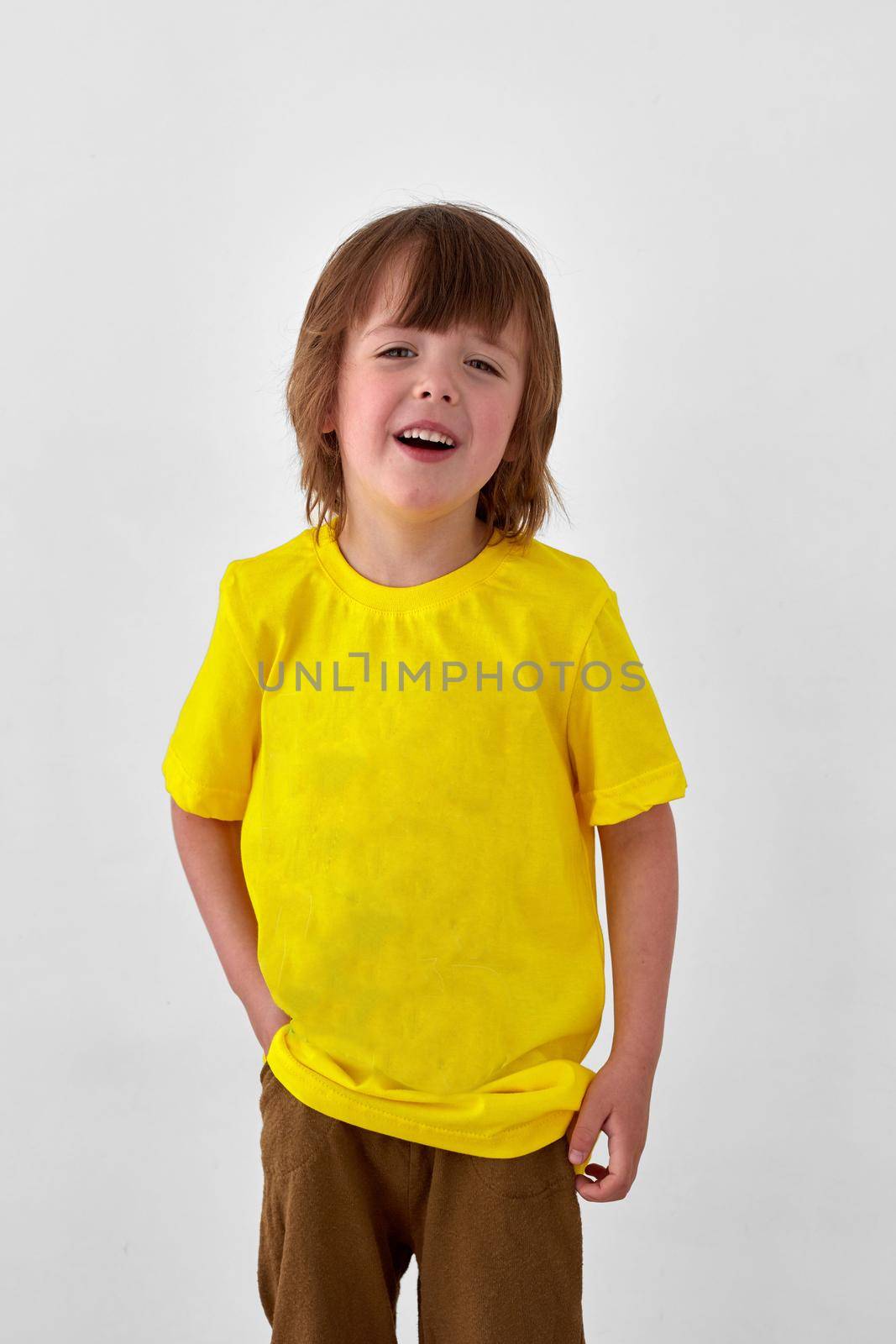 Positive young boy in casual yellow outfit standing on white background by Demkat
