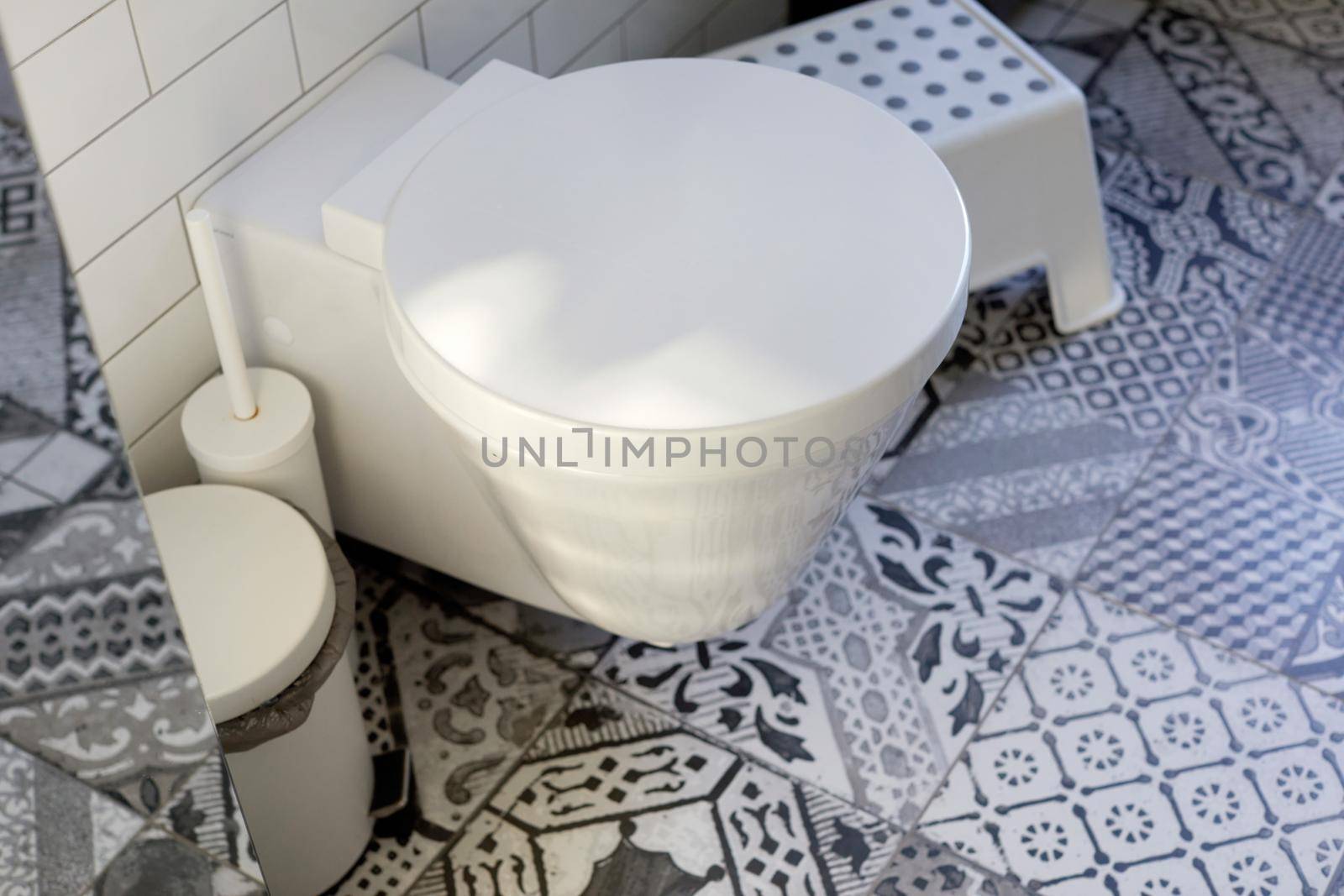 Stylish home interior design of restroom with white toilet bowl and accessories on ornamental tile floor