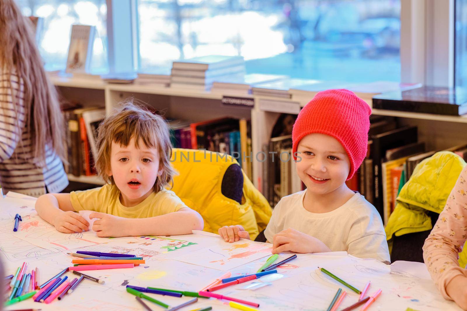 Happy little children drawing with colorful crayons while sitting at table in kindergarten room