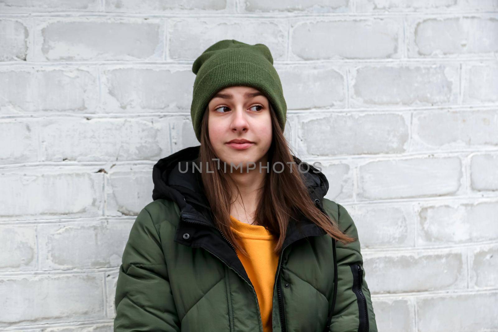 Portrait of a beautiful surprised girl in a yellow sweater and khaki hat, which stands near a white brick wall. The concept of emotions. by lunarts