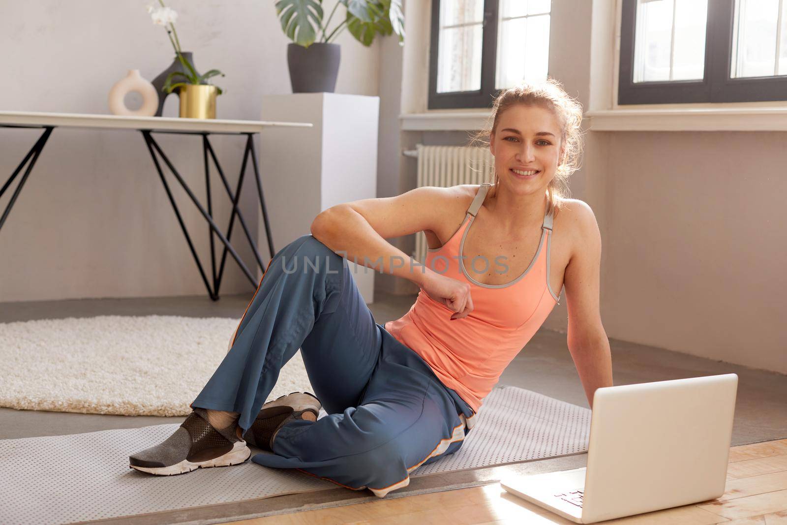 Cheerful sportswoman sitting on mat with laptop by Demkat