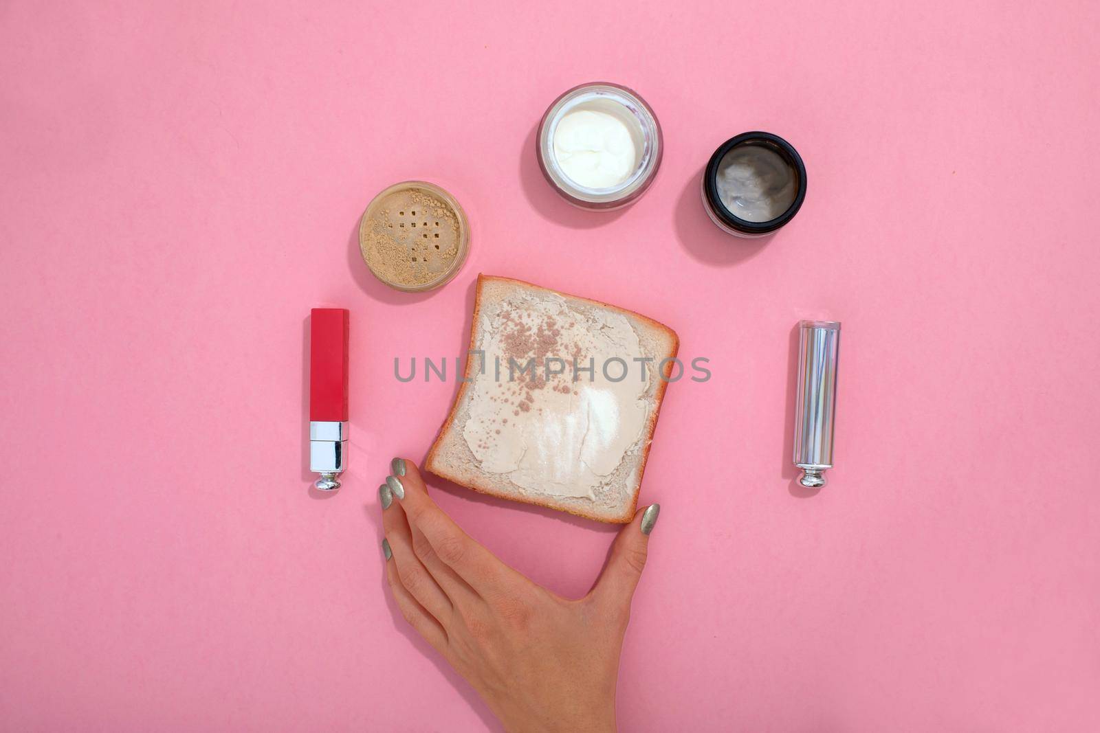 Top view of crop unrecognizable female with toast and various cosmetic products arranged on pink background in studio