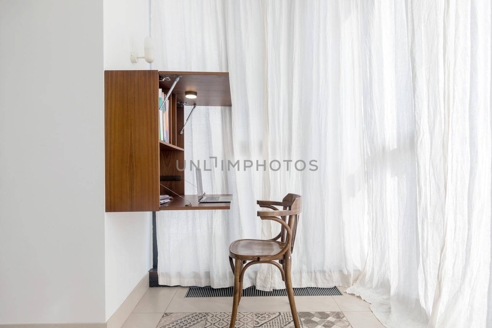 Convenient functional workplace with wooden chair placed near folding shelf with table hanging on wall in modern small area apartment in minimalist style
