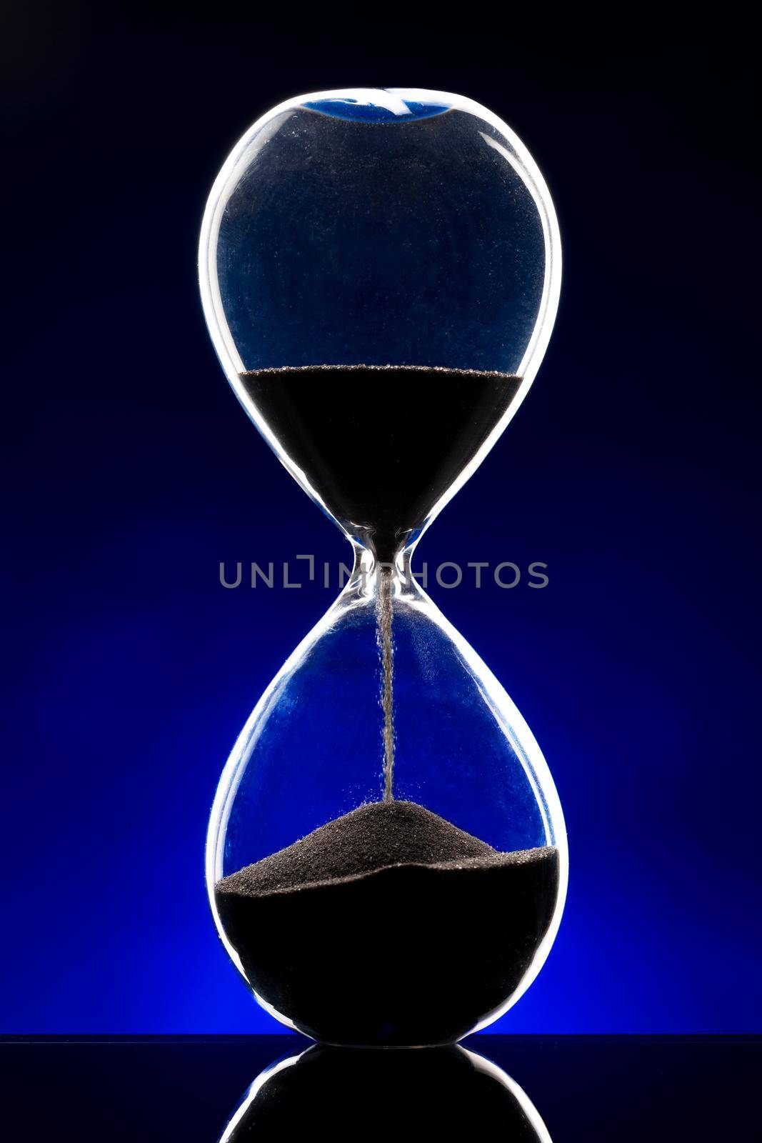 Hourglass illuminated on dark blue background close up photo