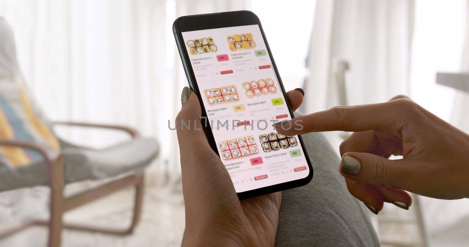 Unrecognizable woman holding phone with app delivery sushi food on screen at home