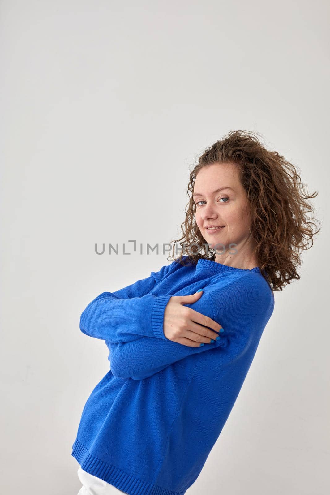Side view of content female wearing trendy blue sweater standing on gray background in studio and looking at camera