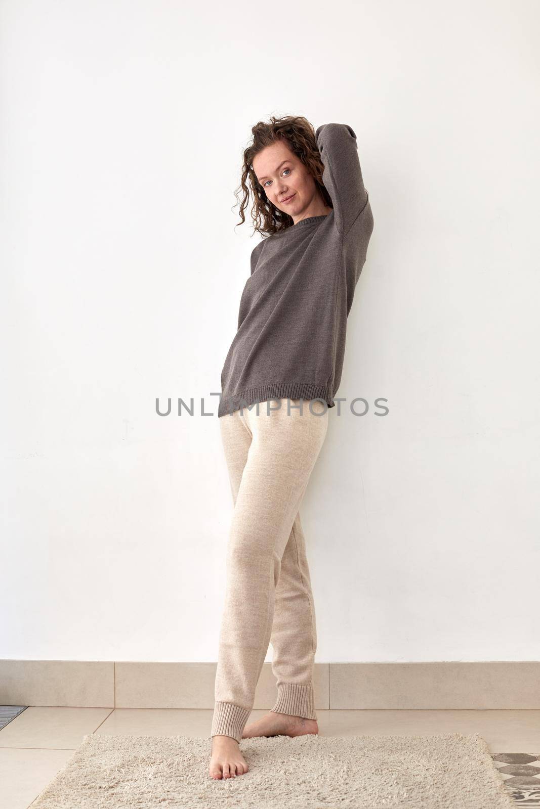 Young woman wearing pullover and pants leaning on white wall by Demkat
