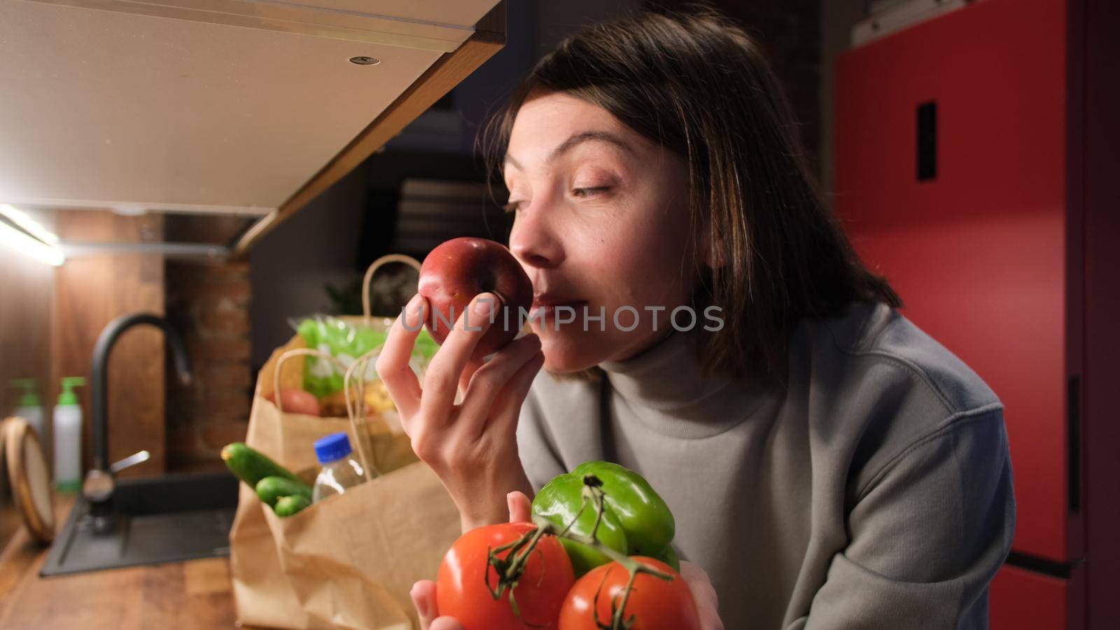Positive lady smelling fresh ripe tomatoes and bell pepper at countertop in kitchen closeup