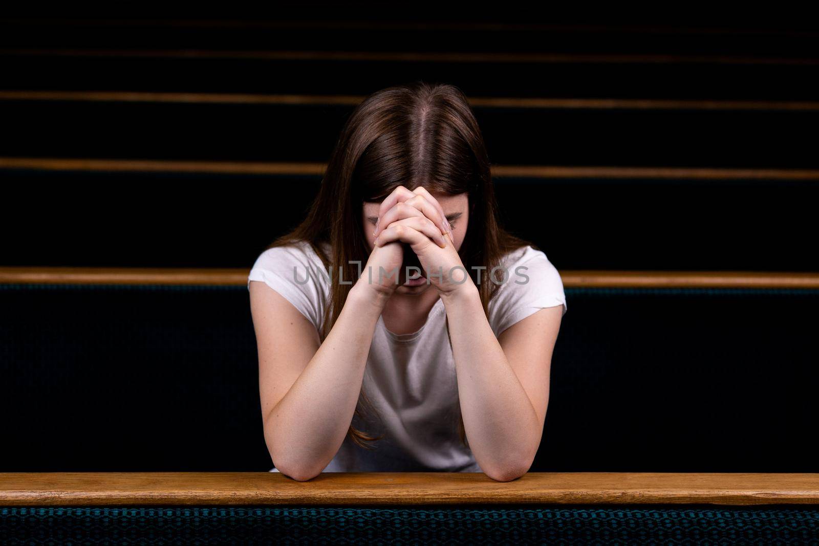 A Sad Christian girl in white shirt is sitting and praying with humble heart in the church.