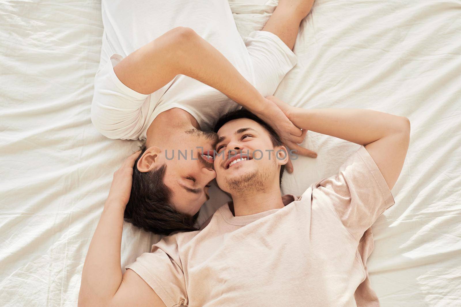 Young gay couple lying on bed tops to tails top view on white sheet