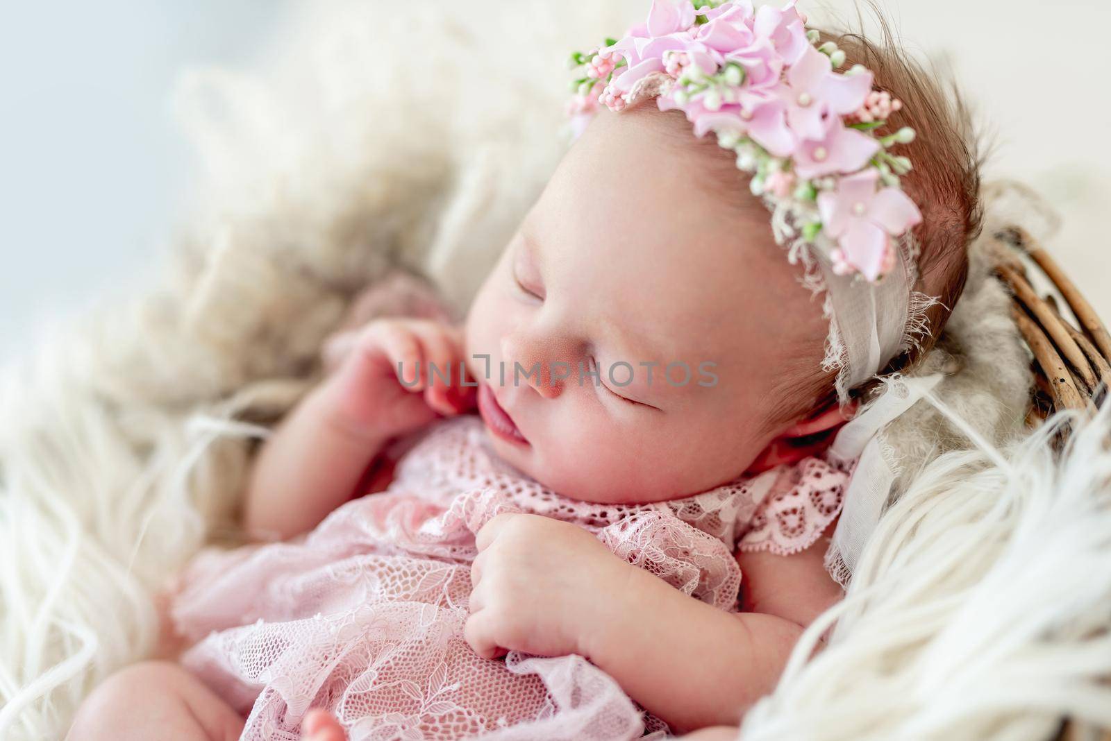 Sleeping newborn baby girl in a pink dress in a basket with flowers