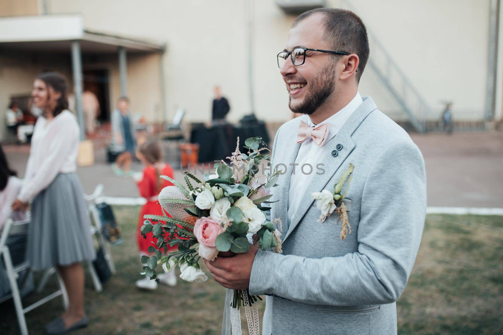 Wedding photo of emotions of a bearded groom with glasses in a gray jacket and rustic style.