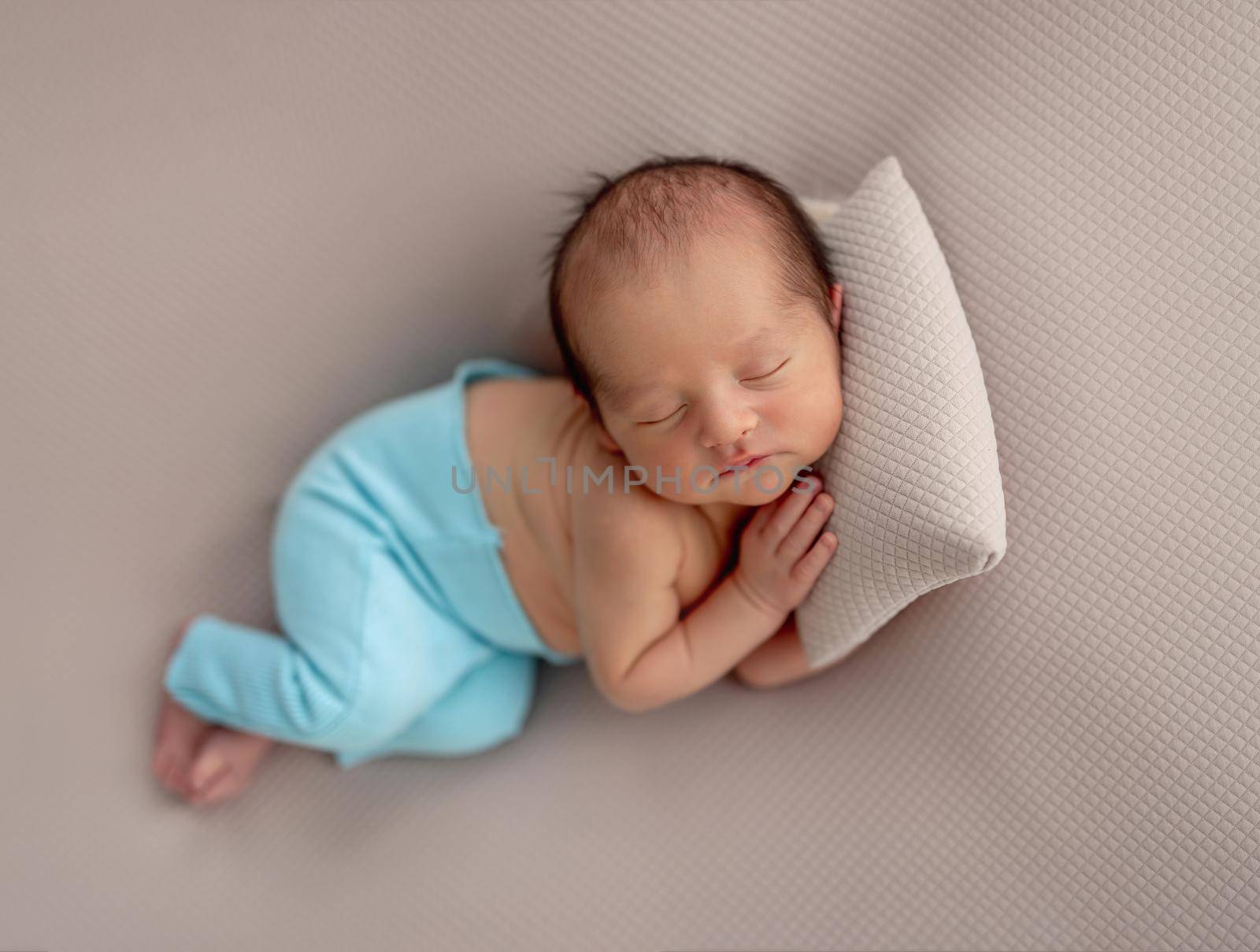 Cute newborn in blue pants sleeping on tiny pillow