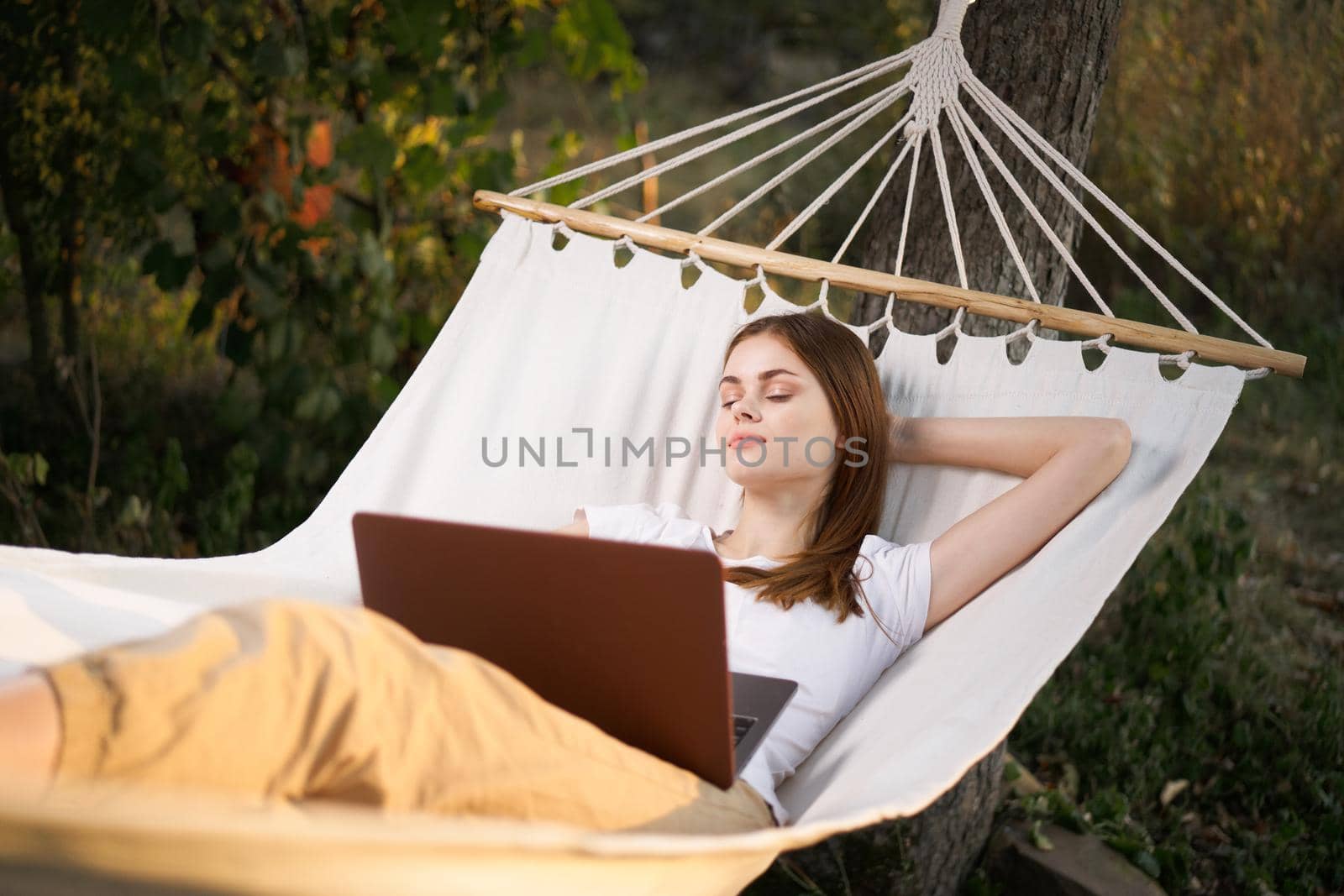 woman outdoors with laptop lies in hammock leisure technology by Vichizh