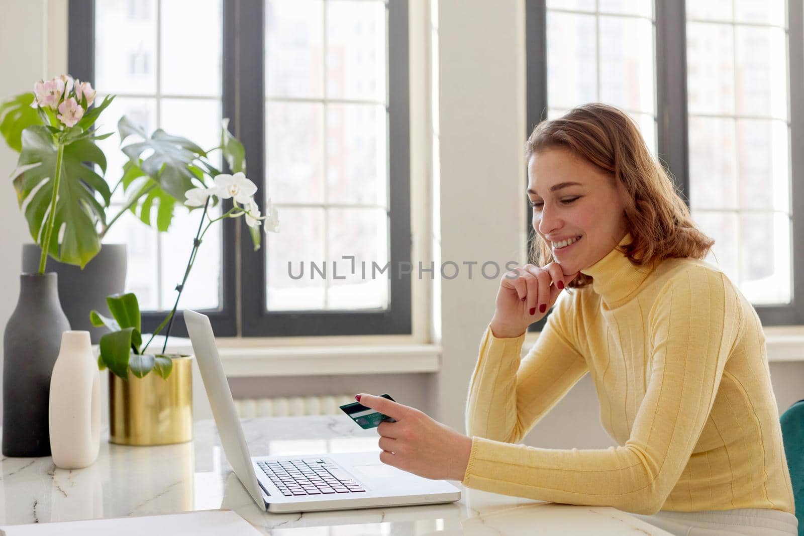Young woman holding credit card and using laptop computer. Businesswoman or entrepreneur working at home. Online shopping, e-commerce, internet banking, spending money, working from home concept