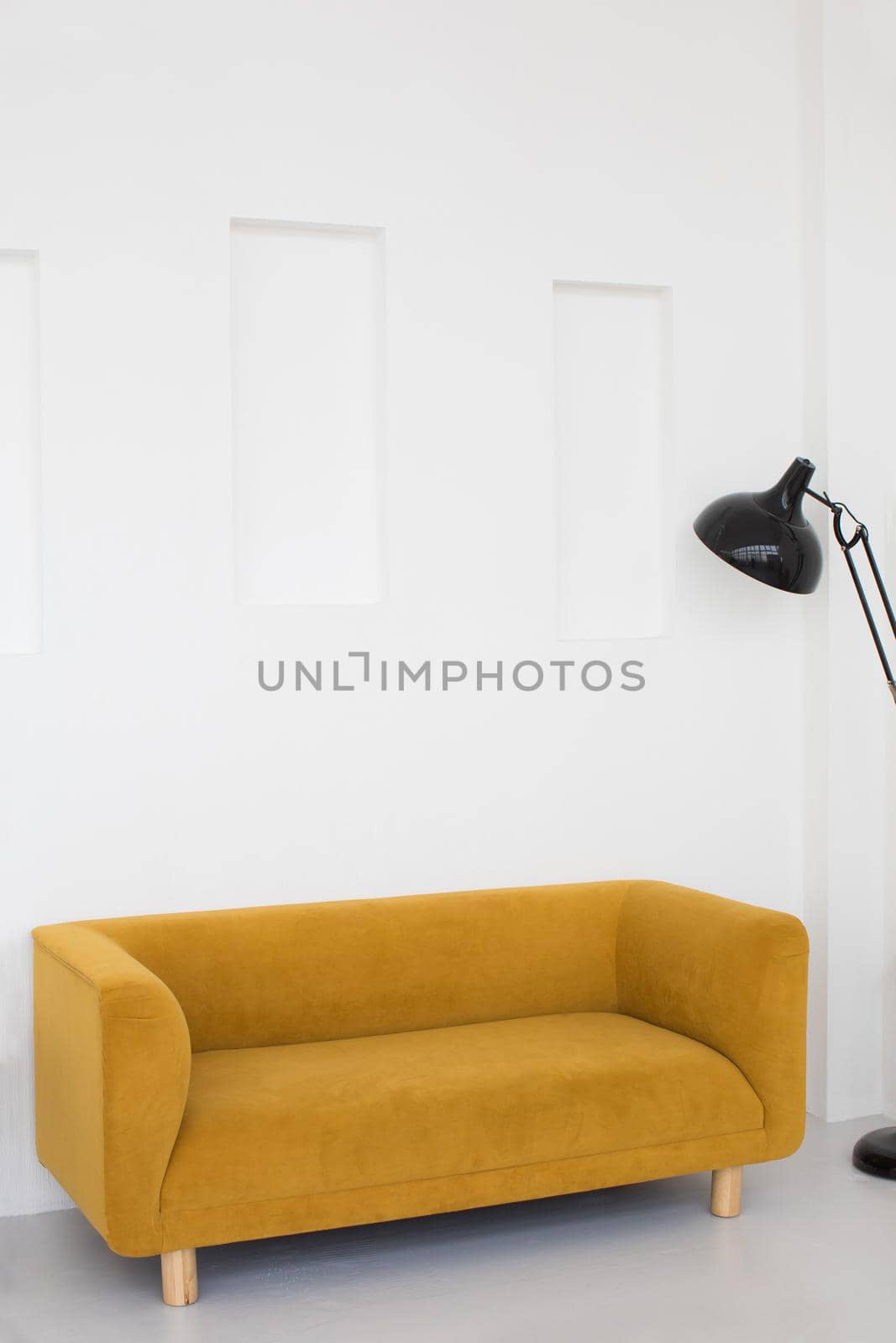 Comfortable yellow couch and floor lamp placed in living room with white walls in minimal style