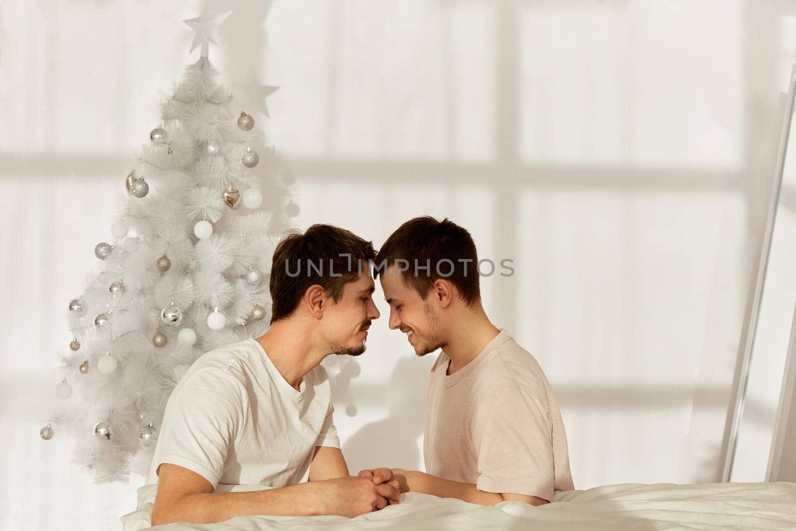 Gay couple forehead touching sitting on the floor by the bed in christmas at home
