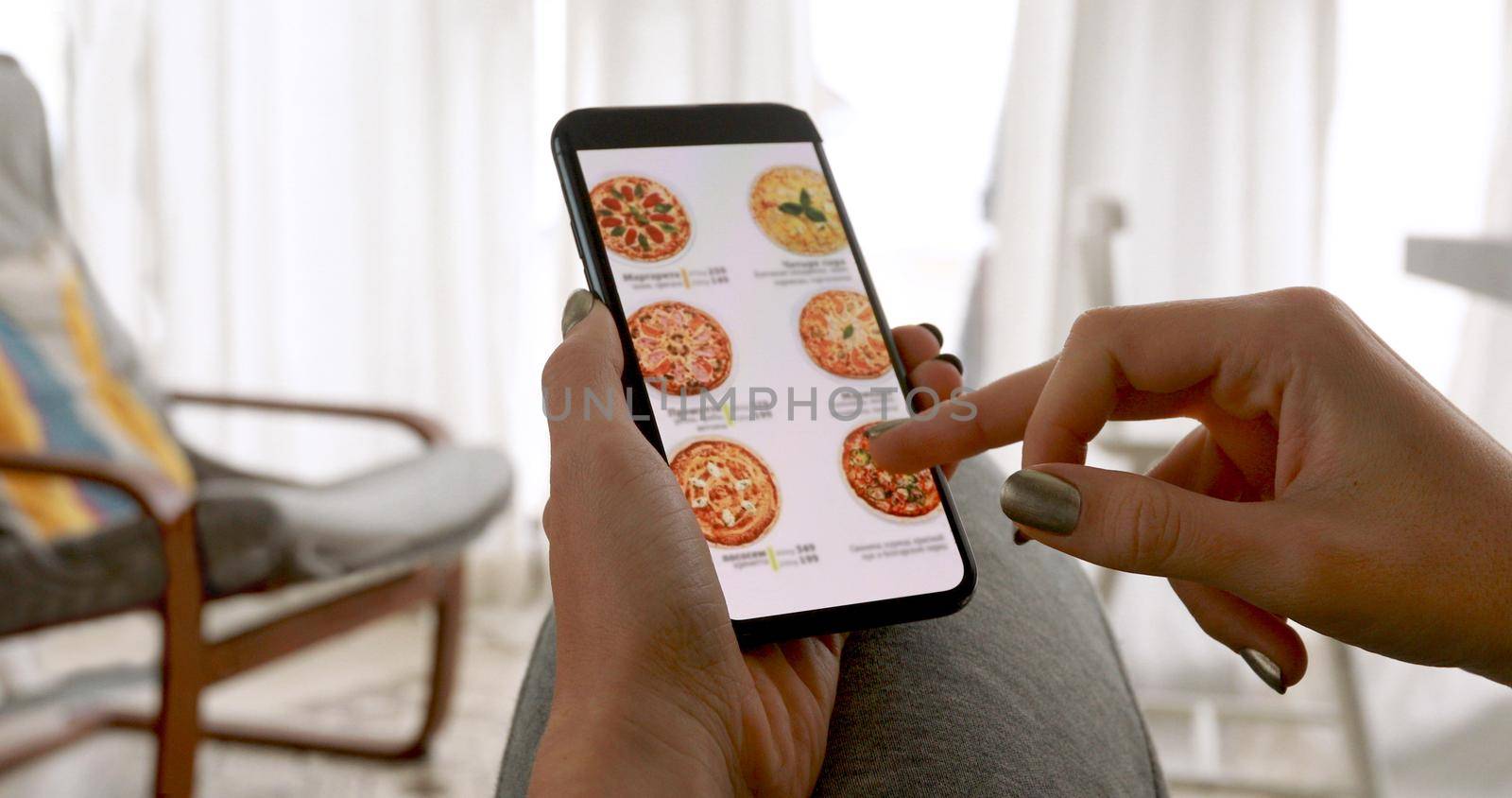 Woman browsing smartphone screen ordering pizza at home online