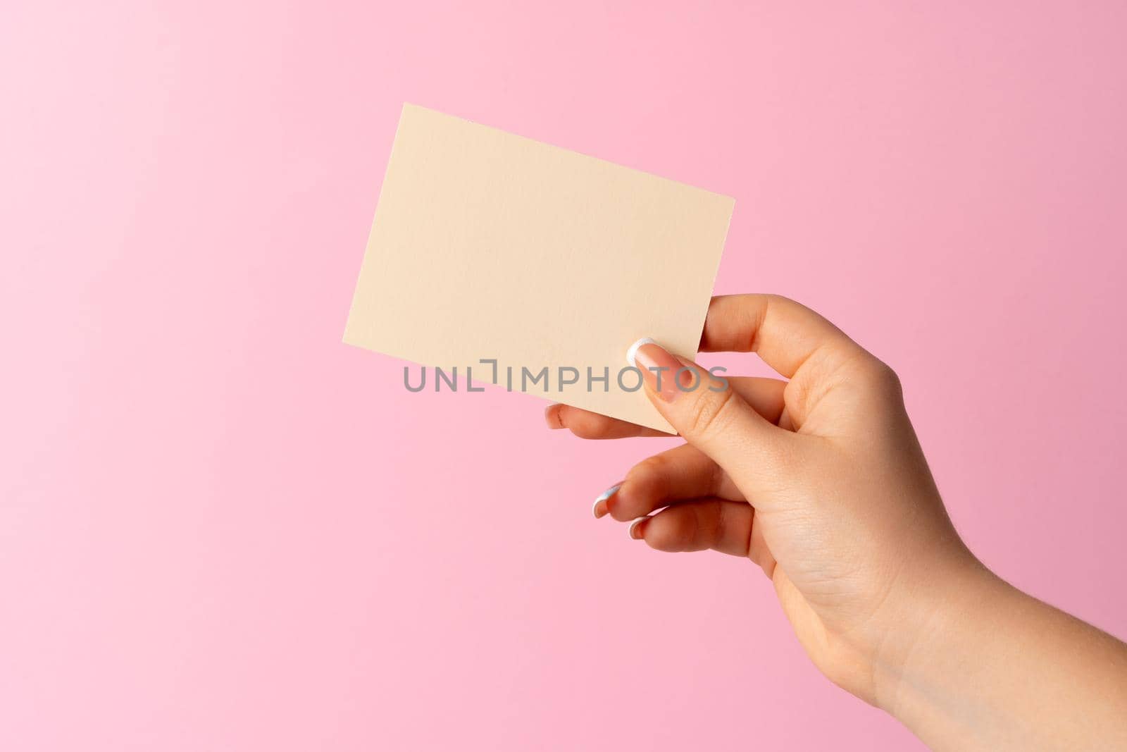 Woman hand showing blank business card on pink background. by Fabrikasimf