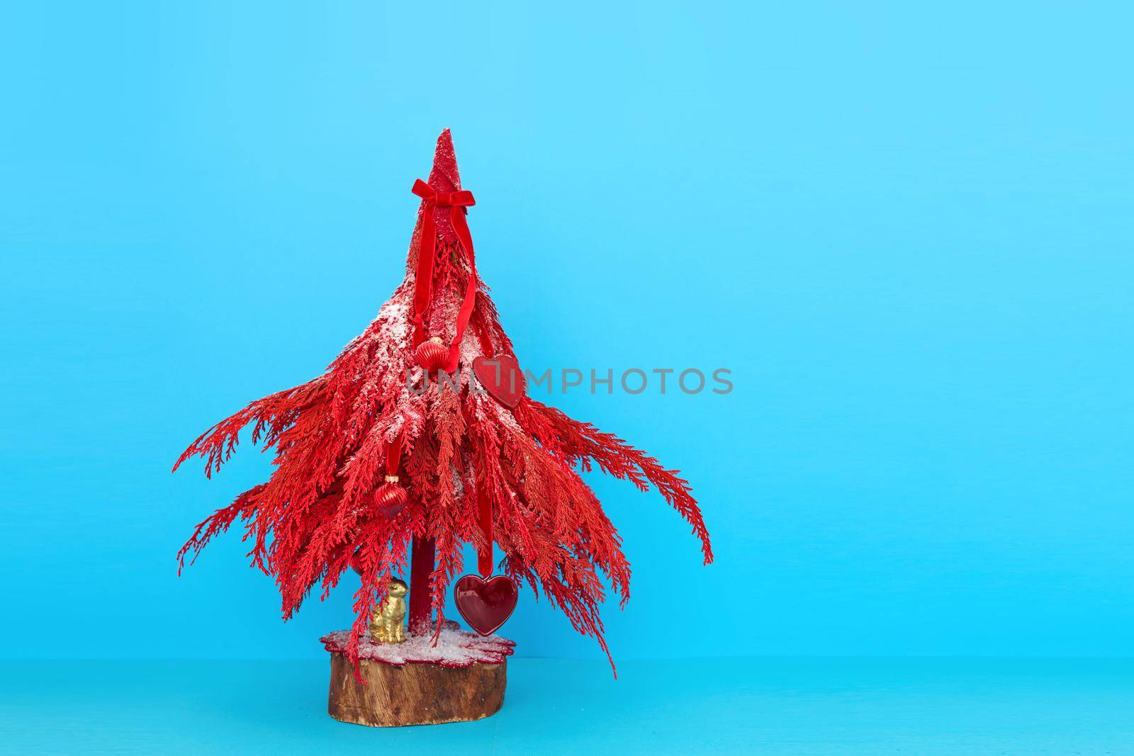 Miniature red decorative Christmas tree with tiny ornaments placed on vivid blue background in studio