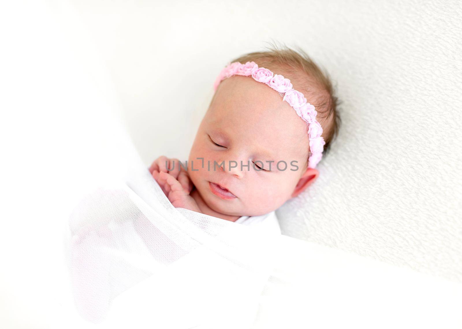 Sleeping newborn baby girl wrapped in white blanket