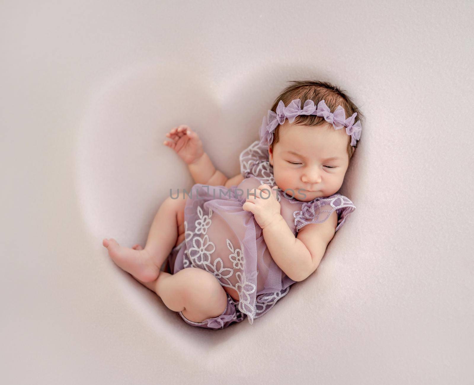 Adorable newborn baby girl wearing beautiful dress and wreath lying in heart shape decoration and sleeping in studio. Cute infant child napping