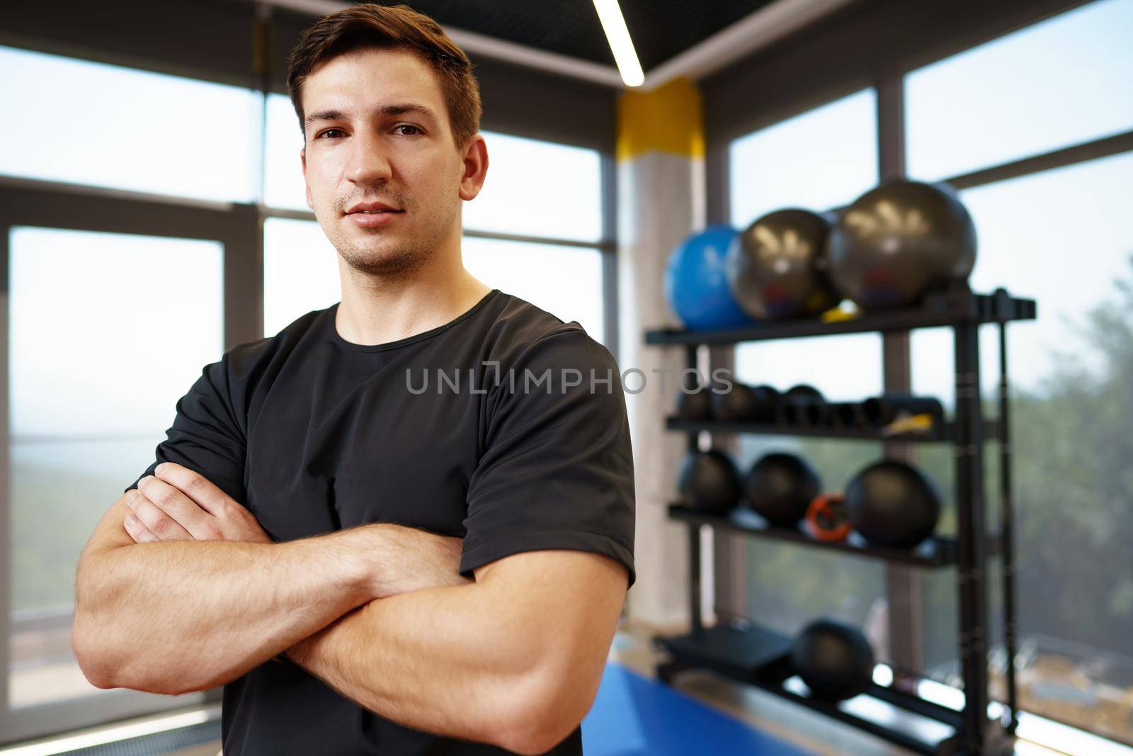 Portrait of a young handsome fitness trainer in a gym by Fabrikasimf