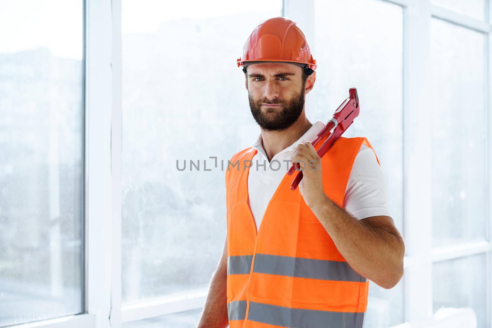 Young male plumber in workwear holding pipe wrench on a construction site indoors