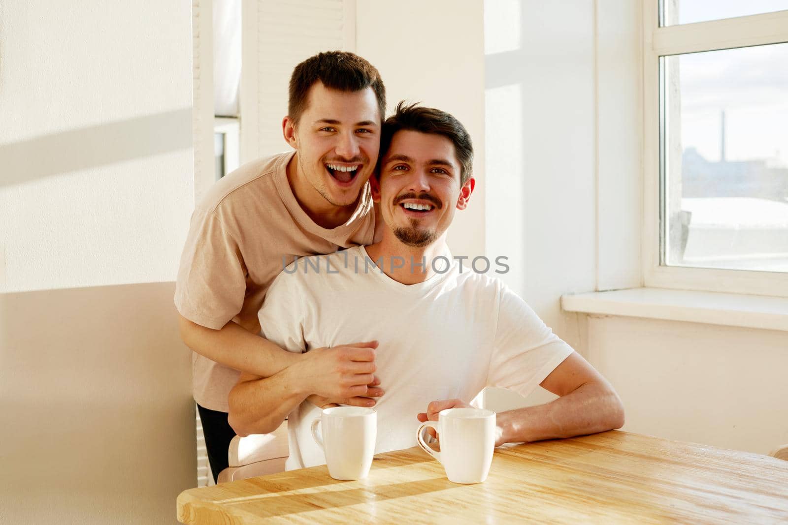 Happy gay couple enjoying hot beverage at home by Demkat