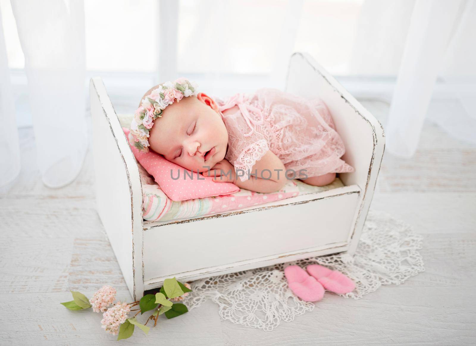 Newborn baby girl wearing cute costume sleeping in the little designed bed and holding her hands under cheek. Beautiful infant child napping lying on her tummy. Pretty kid resting in light room