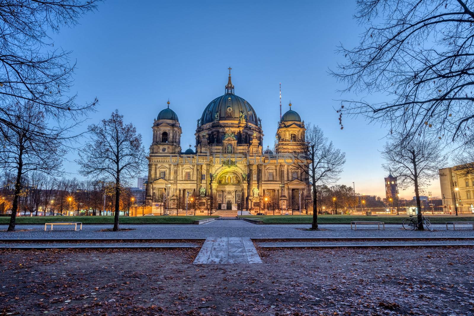 The illuminated Berlin Cathedral in autumn with some barren trees before sunrise