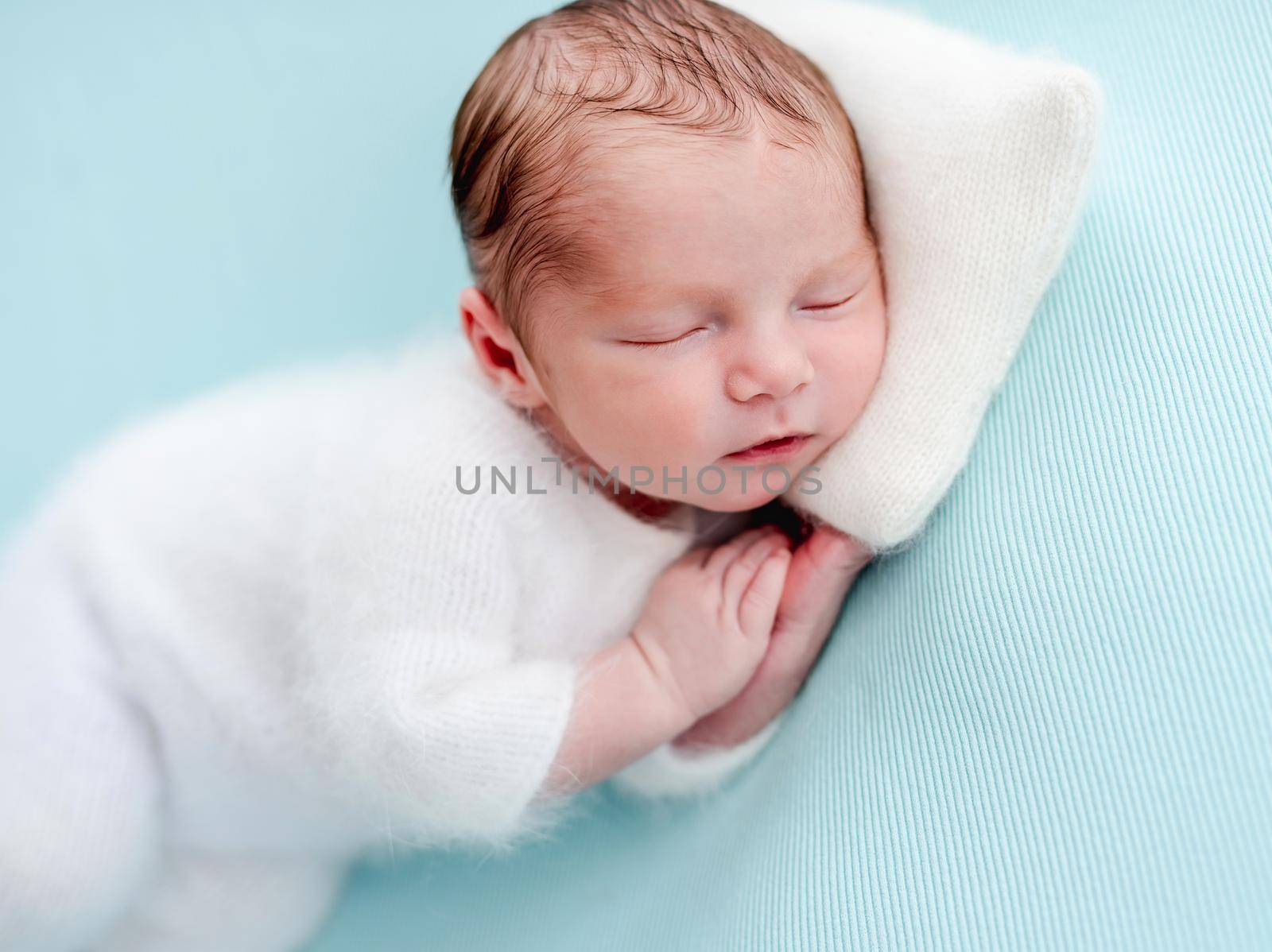 Lovely newborn in white clothes resting with head on tiny pillow