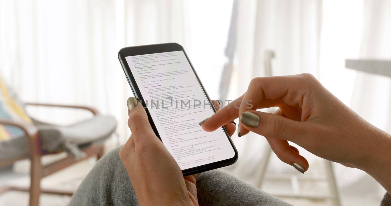 Woman hand using smartphone reading text from smartphone screen. Close-up of young women hand in the living room at home