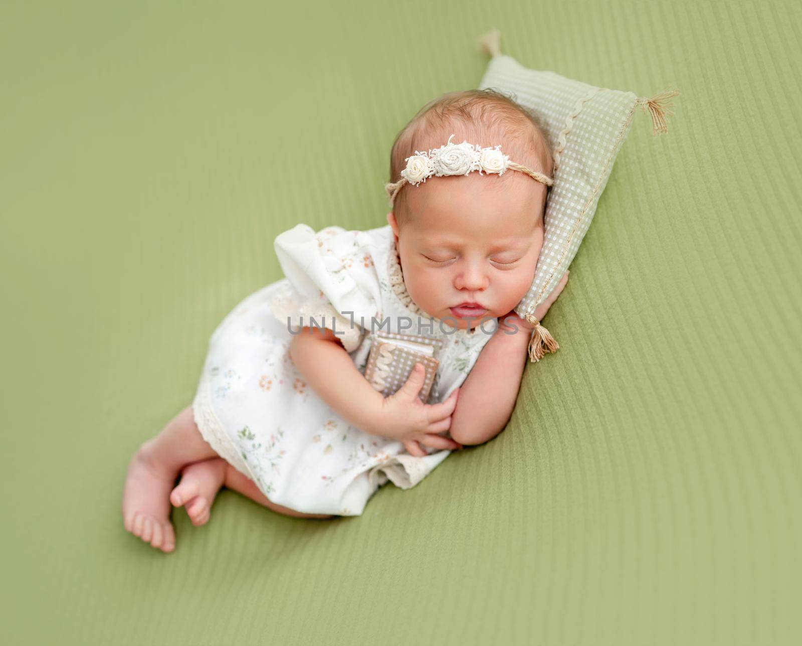 Charming newborn resting on tiny pillow holding small book