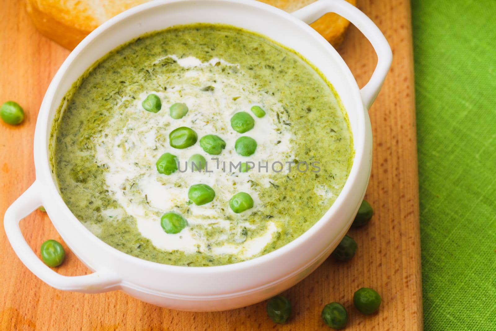 Fresh peas cream soup in a bowl on a wooden board and croutons