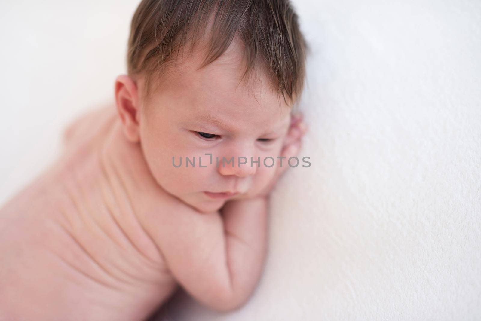 Innocent naked newborn lying awake on stomach