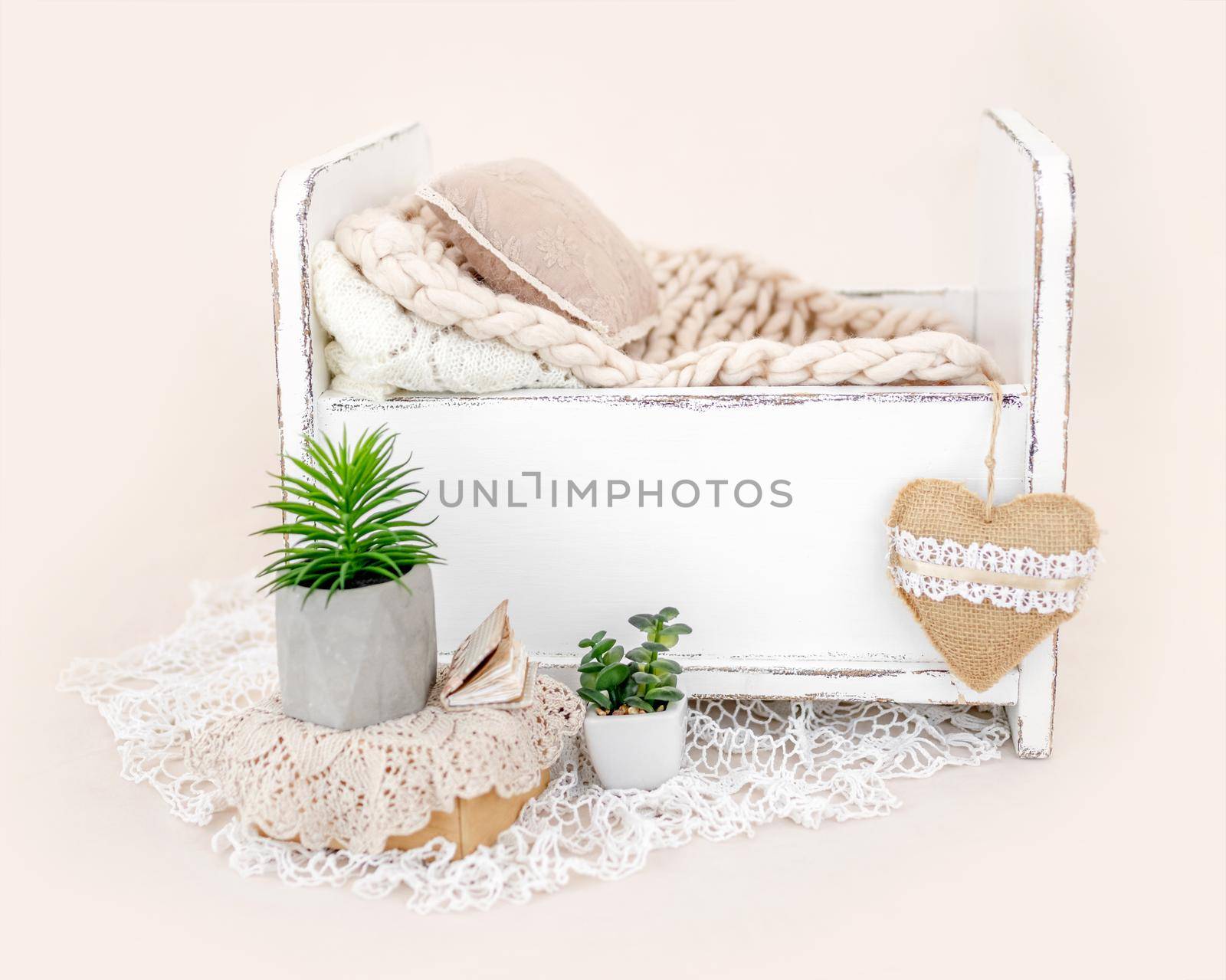 Beautiful white wooden bed furniture for newborn studio photoshoot with fur, pillow decoration. Tiny designed place for infant photo isolated on light pink background