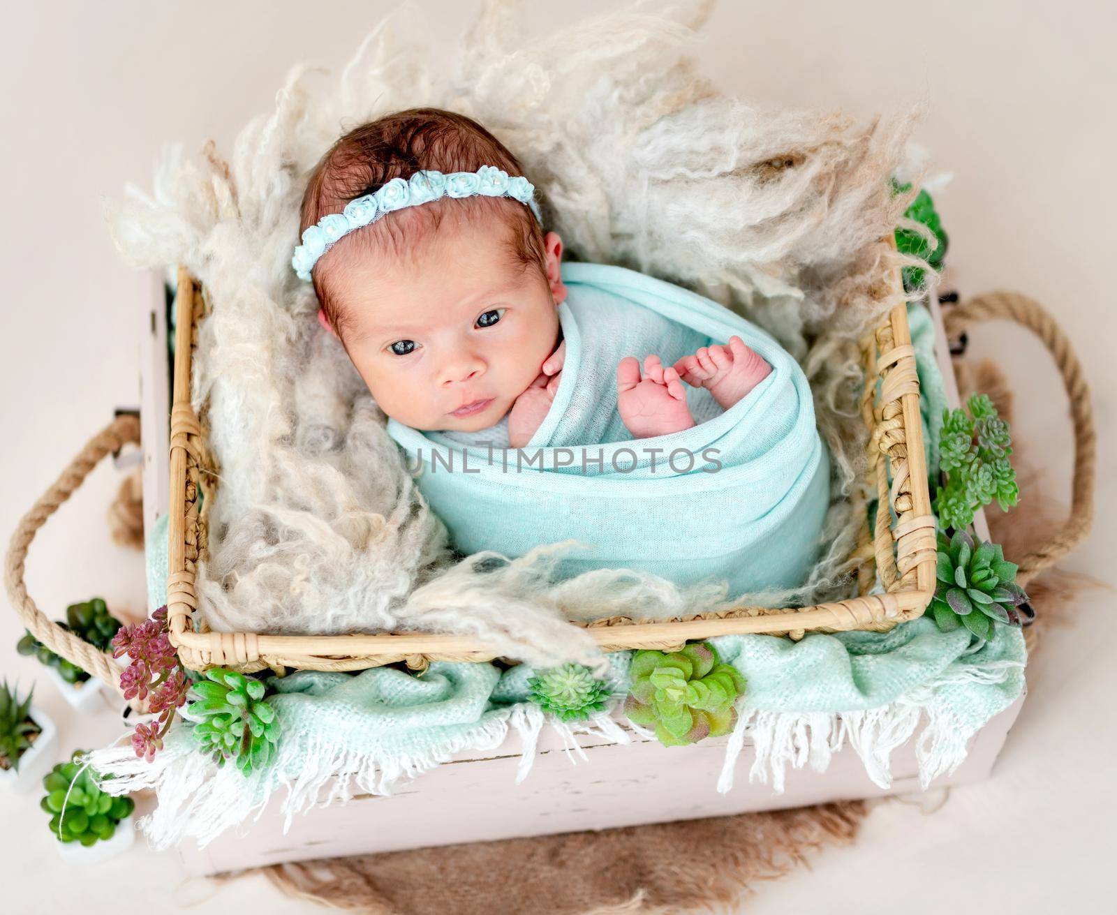 Sweet newborn with open eyes lying in cradle