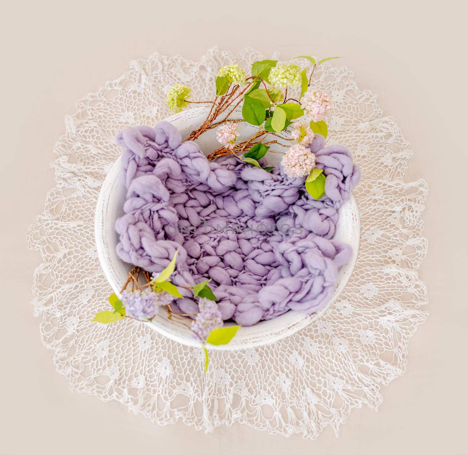 Beautiful backdrop for newborn photosession with flowers hydrangea. Digital composite with basin filled with knitted blanket isolated on light pink background. Top view