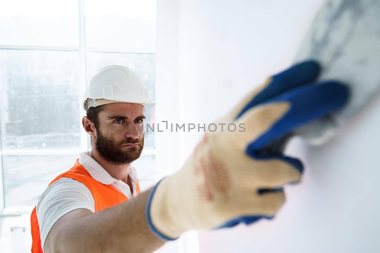 Plasterer in workwear smoothing wall surface of building indoors, close up