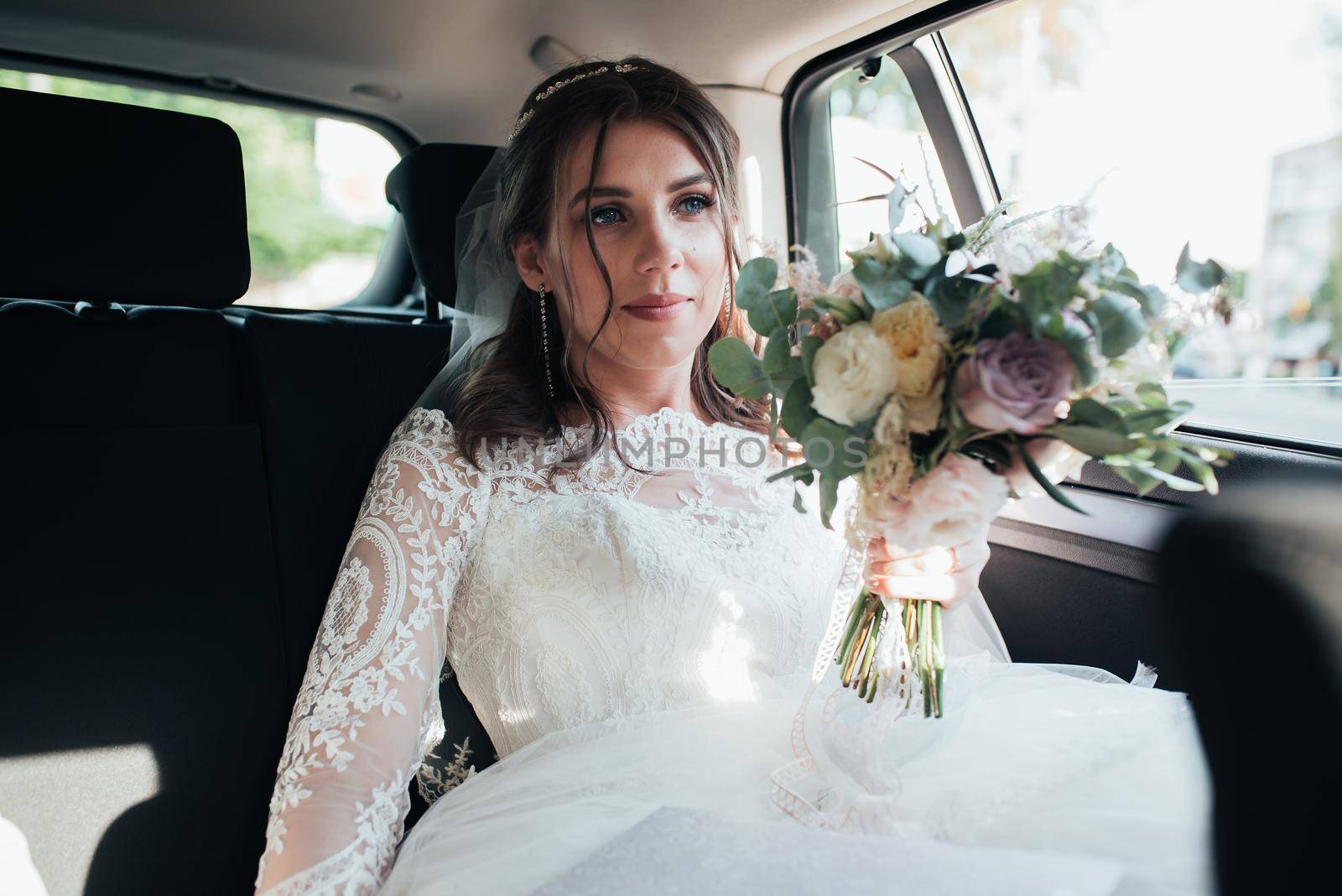 Wedding photo of the bride who is sitting in the car with a bouquet of flowers