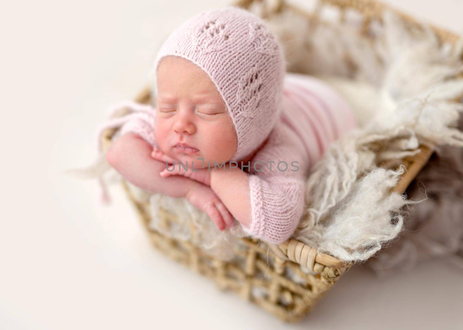 Cute sleeping newborn in basket wearing knitted outfit