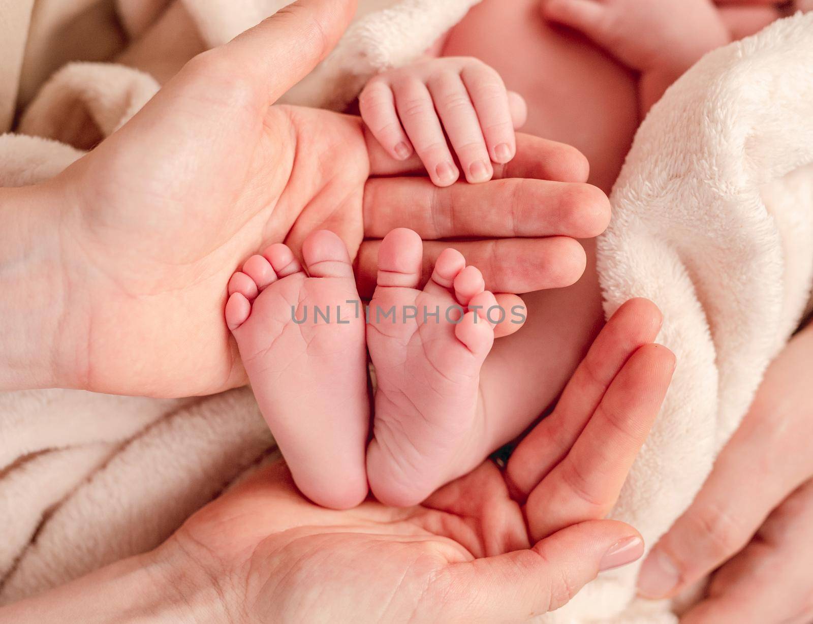 Bare feet of newborn surrounded by family members hands by tan4ikk1