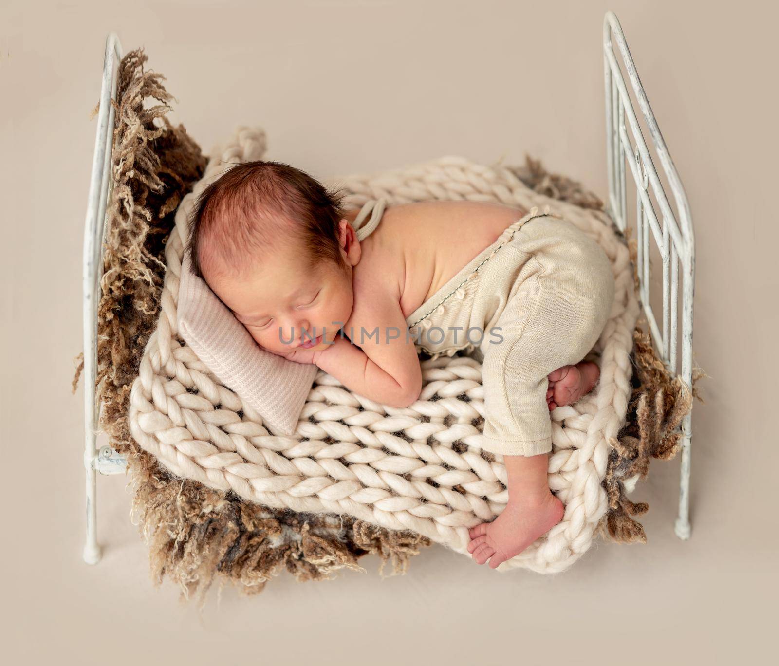 Funny newborn sleeping on tiny bed with pillow